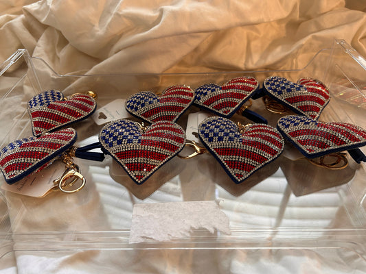 This Wrapables heart keychain features a puffy design adorned with red, white, and blue rhinestones forming an American flag pattern.It includes a gold-toned key ring, a lobster clasp for attachment to purses or handbags, and a dark blue tassel.The heart charm measures approximately 2.5 inches by 2.5 inches.The reverse side is made of a soft plush velvet material.