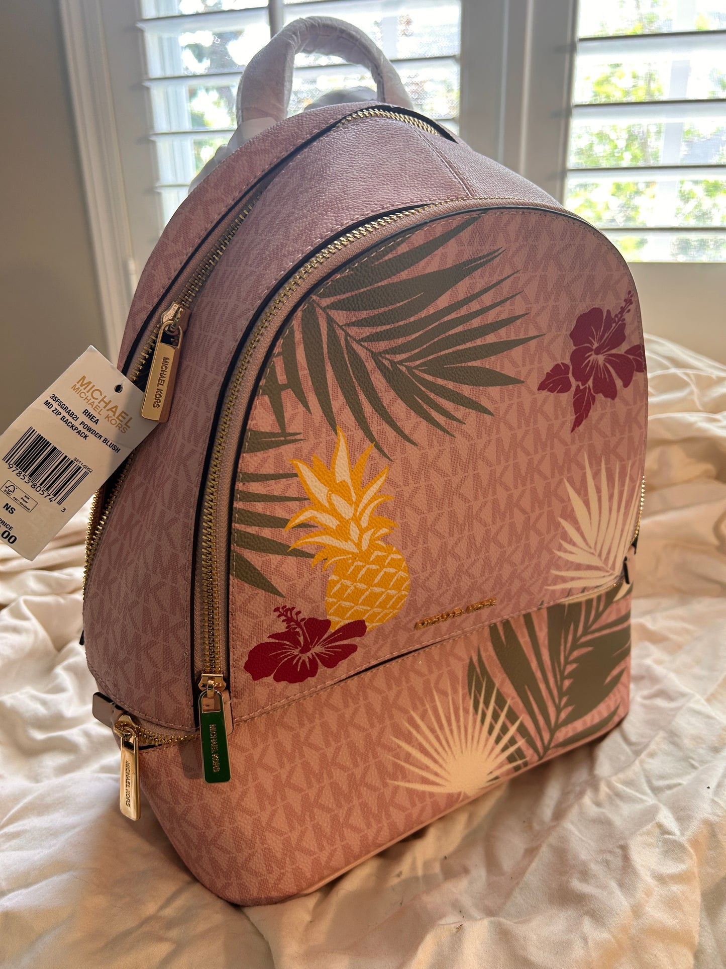 Vibrant, playful print of golden pineapples, lush palm fronds, and hibiscus blooms set against the iconic MK signature logo canvas.

The "Medium" size is the ultimate sweet spot—compact enough for a sleek profile but spacious enough to hold your tablet, wallet, and essentials with ease.Premium 

 Outfitted with gleaming gold-tone hardware and high-quality zip fastenings that offer both luxury and durability. Designed with multiple zippered compartments.