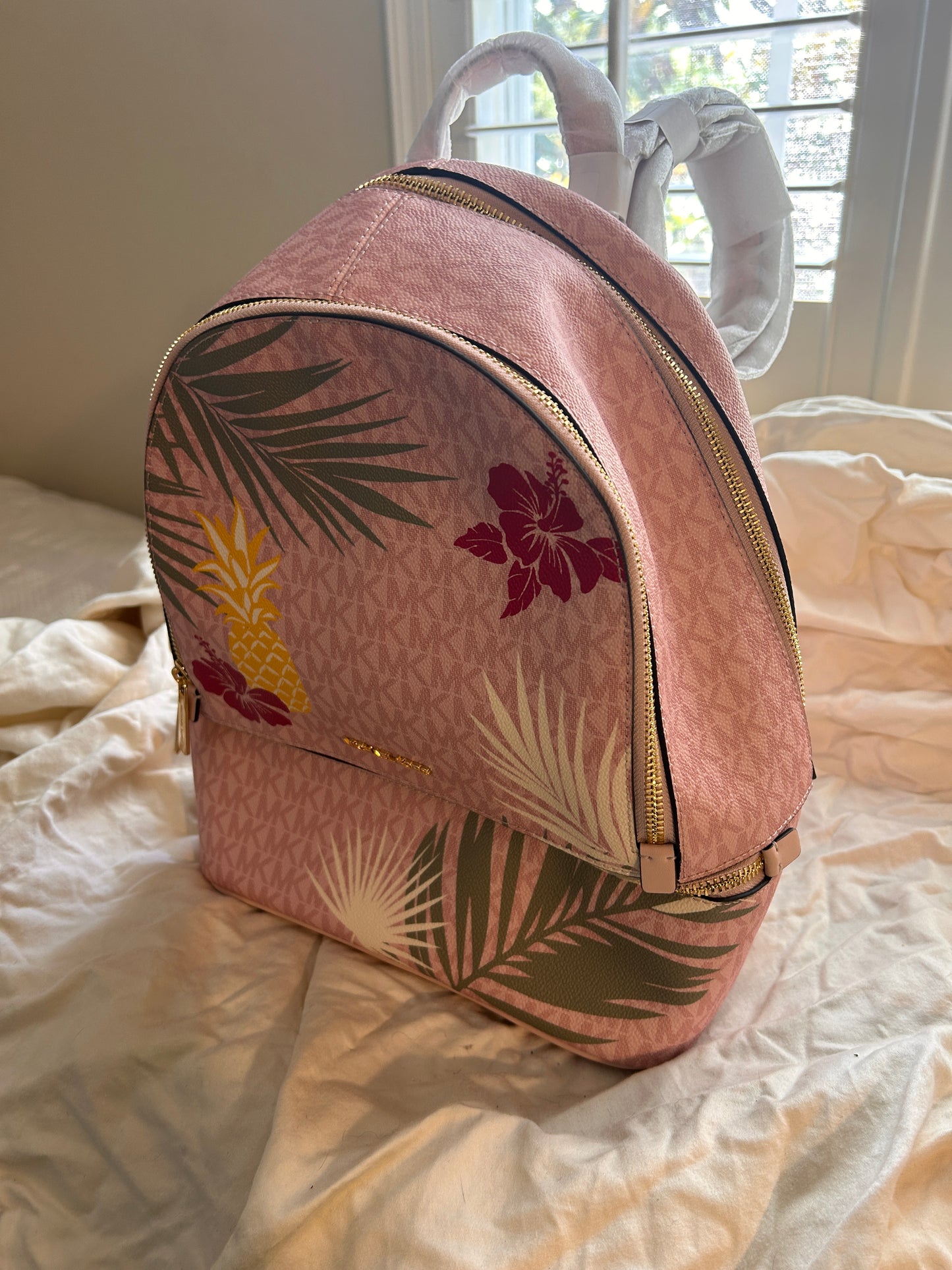Vibrant, playful print of golden pineapples, lush palm fronds, and hibiscus blooms set against the iconic MK signature logo canvas.
 The "Medium" size is the ultimate sweet spot—compact enough for a sleek profile but spacious enough to hold your tablet, wallet, and essentials with ease.
Premium Details: Outfitted with gleaming gold-tone hardware and high-quality zip fastenings that offer both luxury and durability. Designed with multiple zippered compartments.
