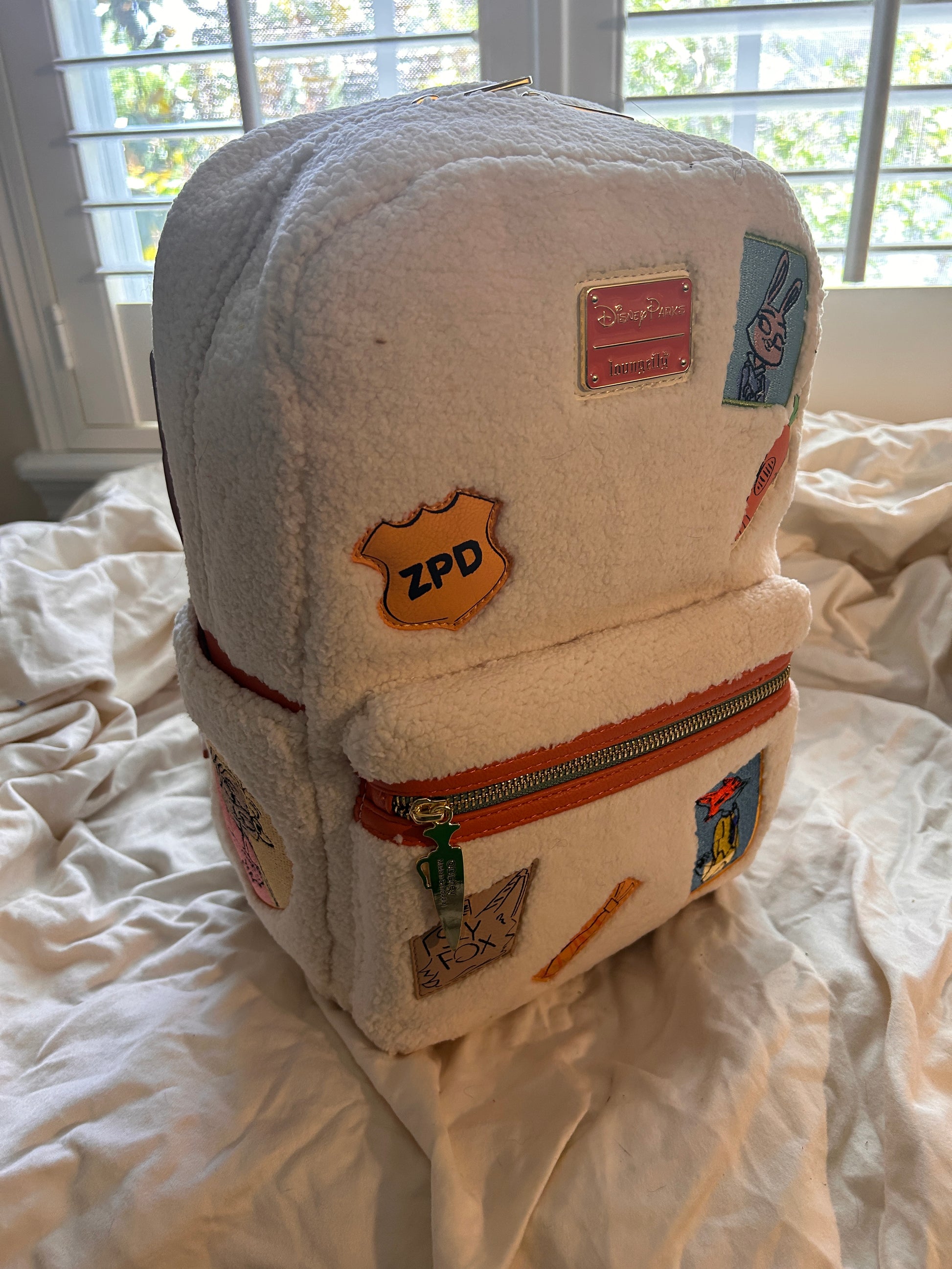 Whimsical Details: Adorned with iconic patches including Judy Hopps, a carrot, and the ZPD badge.

Premium Quality: Crafted with high-quality craftsmanship, featuring a cloisonné Disney Parks x Loungefly metal plate and orange vegan leather trim.Functional Design: Includes a front zip pocket, two side slip pockets featuring sloths Flash and Priscilla, and adjustable padded shoulder straps.

Compact & Durable: Measuring approximately 10.5" H x 9.5" W, it is made of durable polyurethane with a 100% polyester 