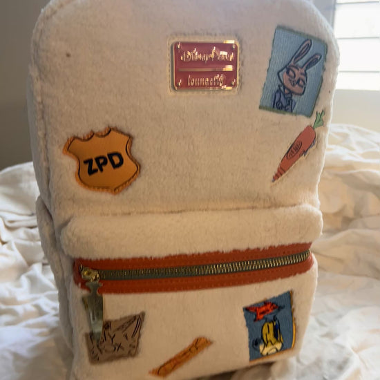 Whimsical Details: Adorned with iconic patches including Judy Hopps, a carrot, and the ZPD badge.
 Crafted with high-quality craftsmanship, featuring a cloisonné Disney Parks x Loungefly metal plate and orange vegan leather trim.

Includes a front zip pocket, two side slip pockets featuring sloths Flash and Priscilla, and adjustable padded shoulder straps.
 Measuring approx 10.5" H x 9.5" W
