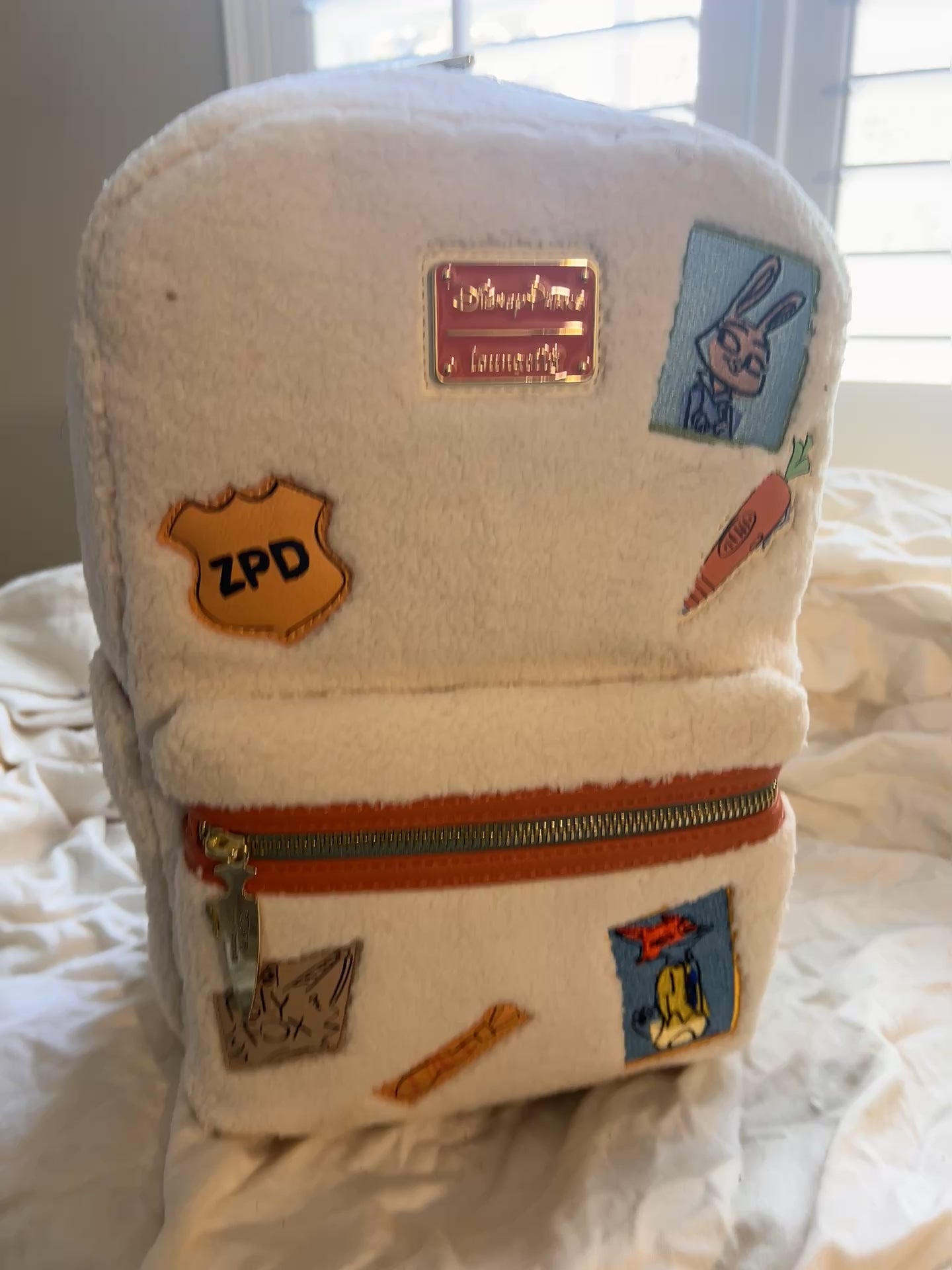 Whimsical Details: Adorned with iconic patches including Judy Hopps, a carrot, and the ZPD badge.
 Crafted with high-quality craftsmanship, featuring a cloisonné Disney Parks x Loungefly metal plate and orange vegan leather trim.

Includes a front zip pocket, two side slip pockets featuring sloths Flash and Priscilla, and adjustable padded shoulder straps.
 Measuring approx 10.5" H x 9.5" W

