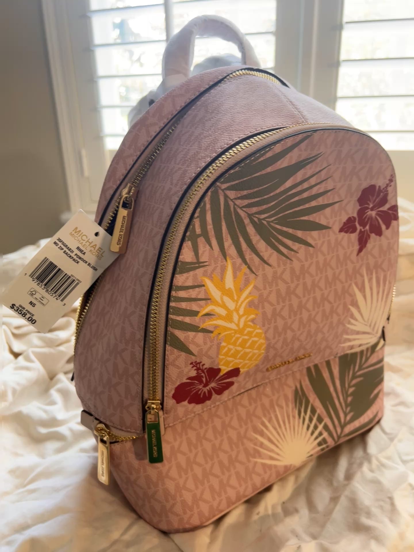 Vibrant, playful print of golden pineapples, lush palm fronds, and hibiscus blooms set against the iconic MK signature logo canvas.
 The "Medium" size is the ultimate sweet spot—compact enough for a sleek profile but spacious enough to hold your tablet, wallet, and essentials with ease.
Premium Details: Outfitted with gleaming gold-tone hardware and high-quality zip fastenings that offer both luxury and durability. Designed with multiple zippered compartments.